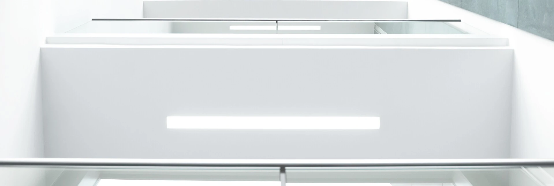 Ein moderner, heller Innenraum mit weißen Wänden und Glasgeländern, der auf eine Treppe hinunterblickt.